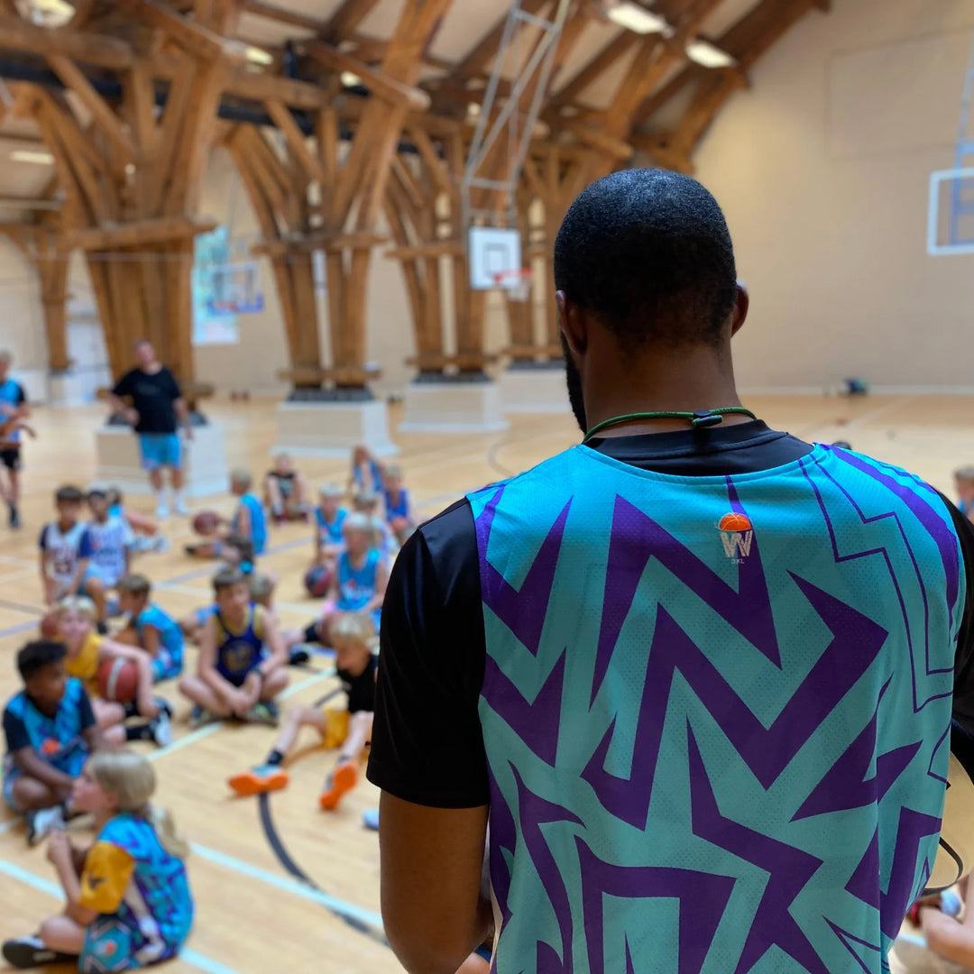 Basketball player in a ZWISH jersey coaching kids seated on court at a ZWISH basketball camp