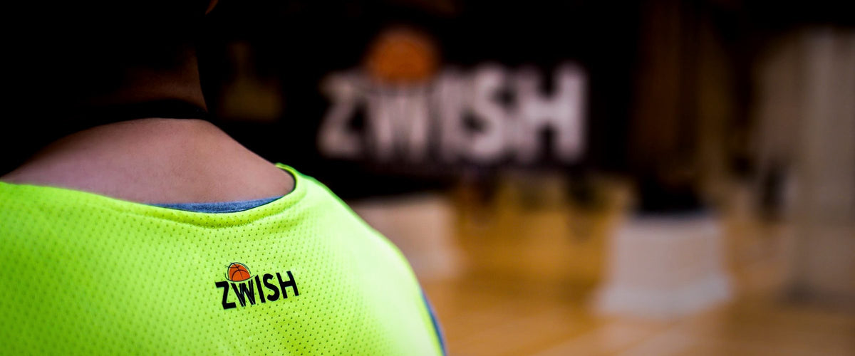 Back of a neon green ZWISH training bib in a blurred gym
