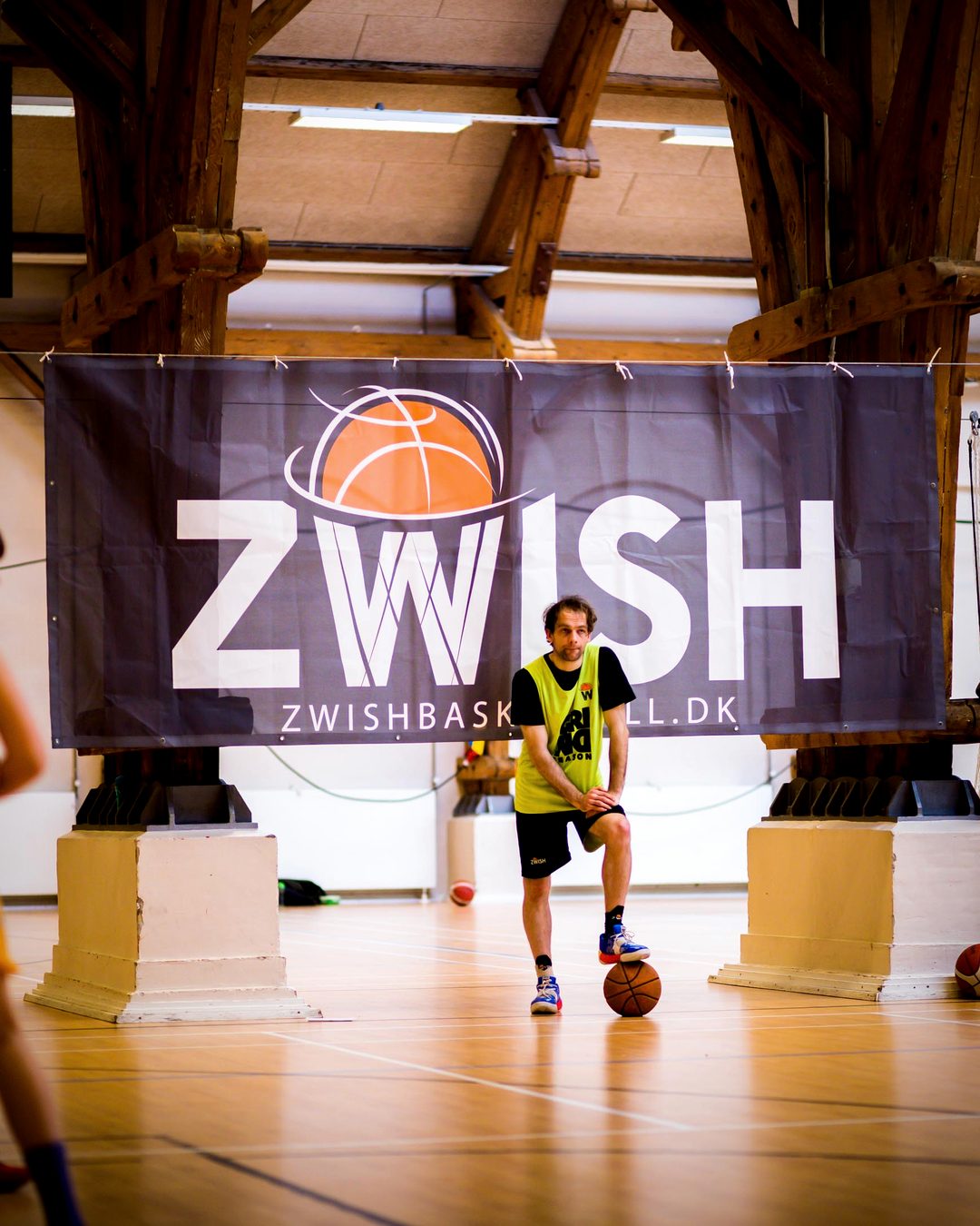 Player dribbling in front of the ZWISH banner in a gym
