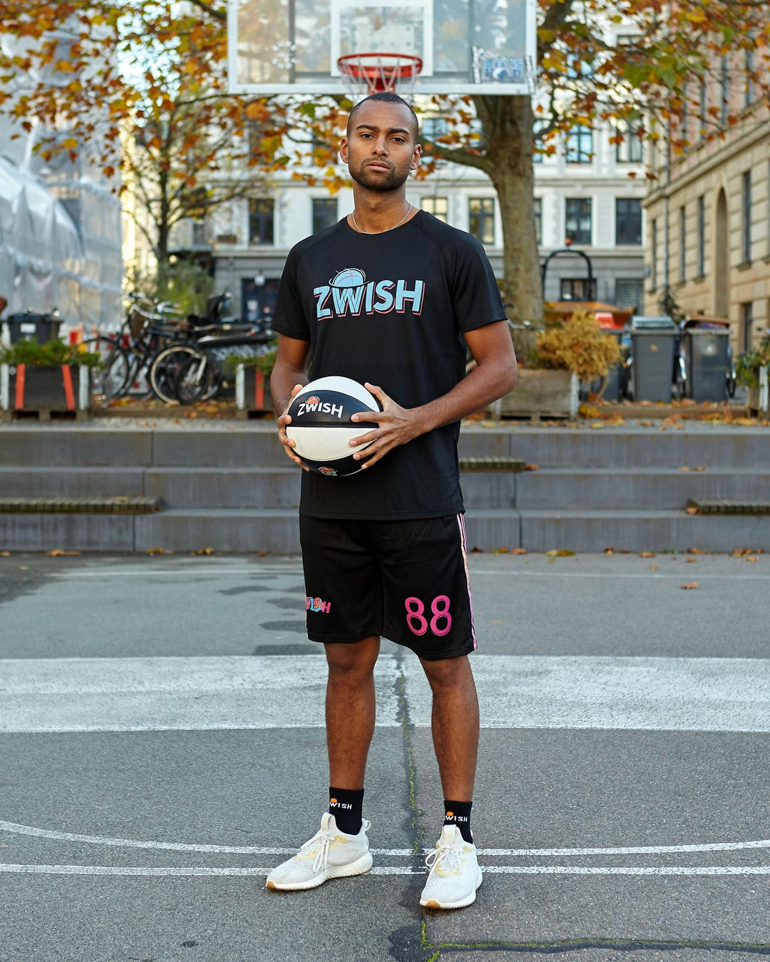 Player in a black ZWISH tee holding a basketball on a Copenhagen street court